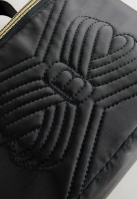 Borsa in tessuto nero trapuntato con un design di cuciture prominenti, una zip dorata e una texture liscia. Forma rettangolare compatta.