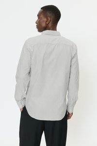 Harmaa-valkoraidallinen pitkähihaispaita, jossa on napillinen kaulus ja pyöristetty helma. Paidassa on kalvosinvarret ja normaali istuvuus.