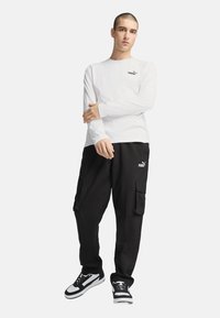 Hvid langærmet skjorte med sort logo, kombineret med sorte cargo bukser med sidelommer og sort-hvide sneakers.