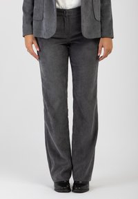 Pantaloni in corduroy grigi con un design a gamba larga, texture a coste e chiusura con bottone in vita. Abbinati a scarpe nere.