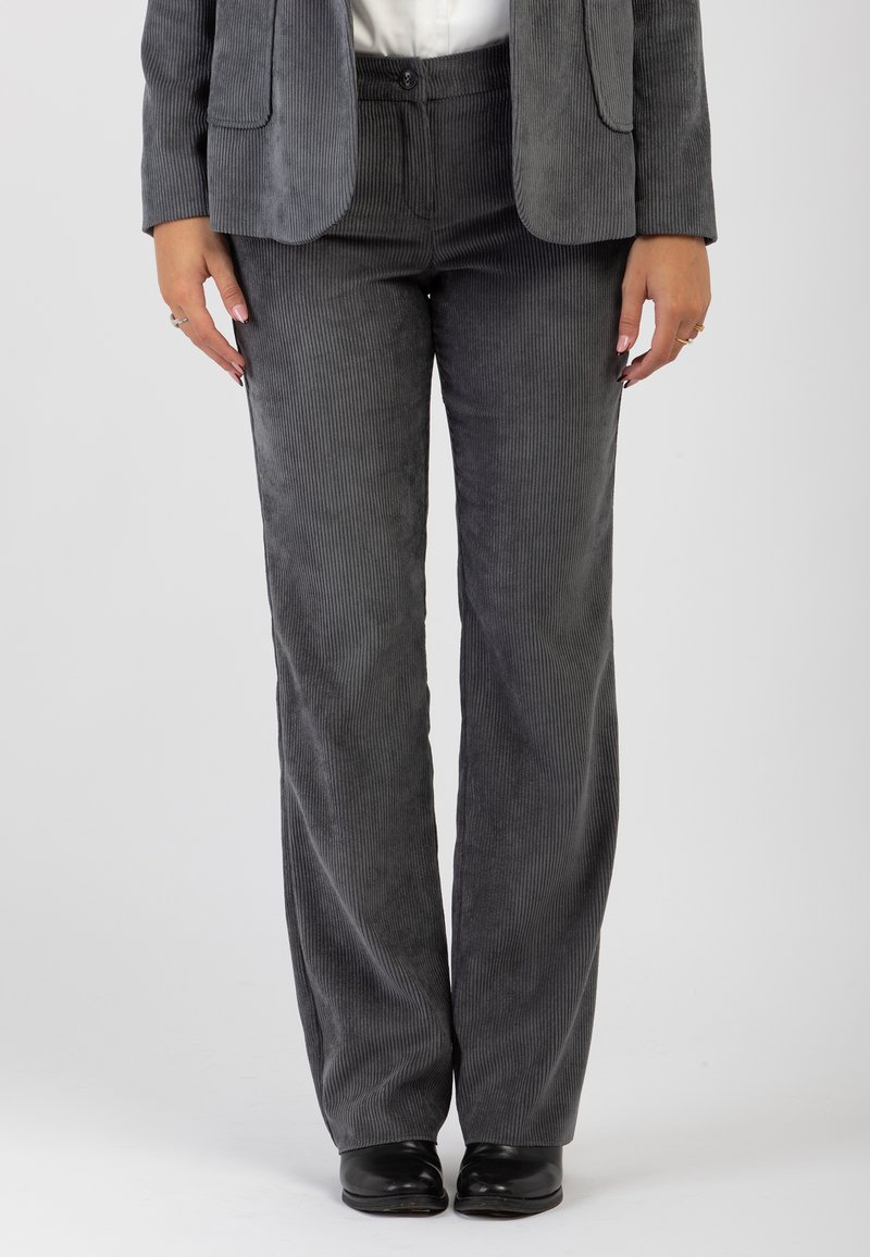 Pantaloni in corduroy grigi con un design a gamba larga, texture a coste e chiusura con bottone in vita. Abbinati a scarpe nere.
