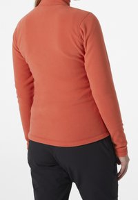 Haut en polaire orange, avec un col montant et des manches longues. Texture lisse avec des coutures plates et un design ajusté.