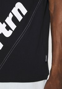 Černé tričko s bílým diagonálním textem, kontrastním šitím, krátkými rukávy a božním štítkem s nápisem "YOURTURN".