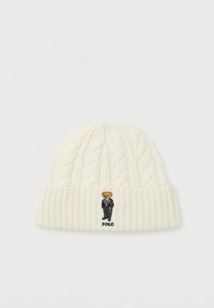 Creamkleurige kabelgebreide beanie met omgevouwen rand, voorzien van een geborduurde teddybeer in een zwart pak en de tekst "POLO" eronder.