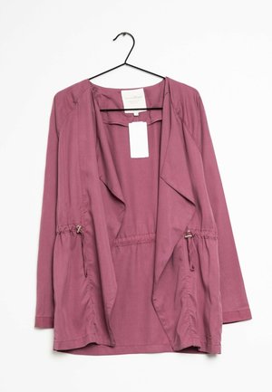 Kurtka z długim rękawem w kolorze mauve, z otwartym przodem i regulowanymi sznurkami po bokach, wisząca na czarnym wieszaku na białym tle.