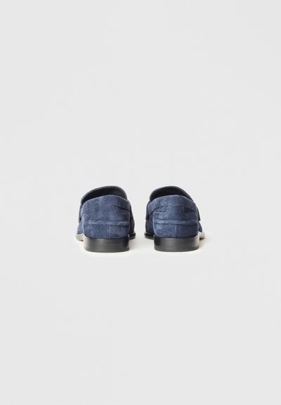 Granatowe zamszowe mokasyny z czarną, płaską podeszwą; posiadają przeszywane detale i wsuwany fason. Widok z tyłu ukazuje gładką teksturę.