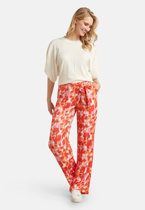 Lichte crèmekleurige top met korte, brede mouwen, gecombineerd met oranje en roze bloemenprint, wijde broek met een trekkoord in de taille en een gladde textuur.