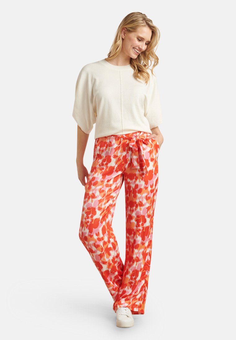 Hellbeige Oberteil mit kurzen, weiten Ärmeln, kombiniert mit orangen und rosafarbenen Blumenmustern, dazu weite Hose mit Kordelzugbund und glatter Textur.