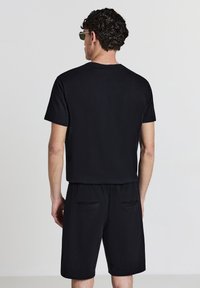 Schwarzes T-Shirt mit kurzen Ärmeln kombiniert mit passenden schwarzen Shorts. Das Outfit hat eine lockere Passform und verfügt über zwei Gesäßtaschen an den Shorts.