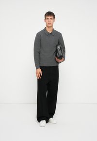 Suéter gris de punto con cuello, pantalones negros de pierna ancha y zapatillas blancas. Sosteniendo un pequeño bolso de cuero negro. Diseño simple, colores neutros.