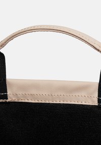 Sac en tissu noir avec une poignée beige. Le dessus présente une bordure cousue, contrastant avec le matériau noir texturé sur les côtés.