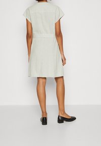 Ljussgrå knälång klänning med kappärmar, insvängd midja och slät textur. Matchad med svarta lågklackade skor.