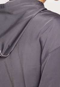 Hooded garment in dark gray, made from smooth, lightweight fabric. Features a relaxed fit with visible texture and contrasting stitching.