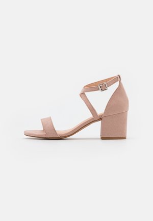 Beige suede open-toe sandal with block heel and ankle strap featuring a silver buckle, shown in side profile on a white background.
