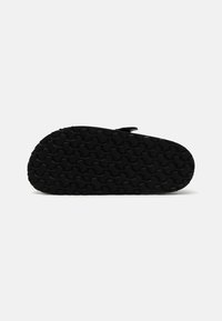 Semelle de chaussure en caoutchouc noir avec un motif de grip texturé, présentant une forme arrondie et un léger arc pour le soutien. Détails minimaux.