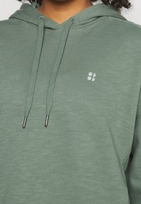 Felpa verde in cotone con una finitura testurizzata, caratterizzata da un piccolo logo e dettagli in argento sui cordini. Vestibilità morbida e rilassata.