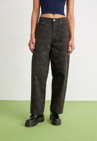 Bredde ben jeans i mørkegrøn jacquard-stof med blomsterprint, med høj talje, metal knaplukning og fem lommer. Sorte platform støvler.