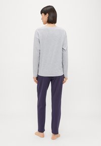 Sivý top s dlhým rukávom v uvoľnenom strihu v kombinácii s tmavofialovými nohavicami. Tkaniny vyzerajú mäkké, ponúkajúce ležérny a pohodlný vzhľad.