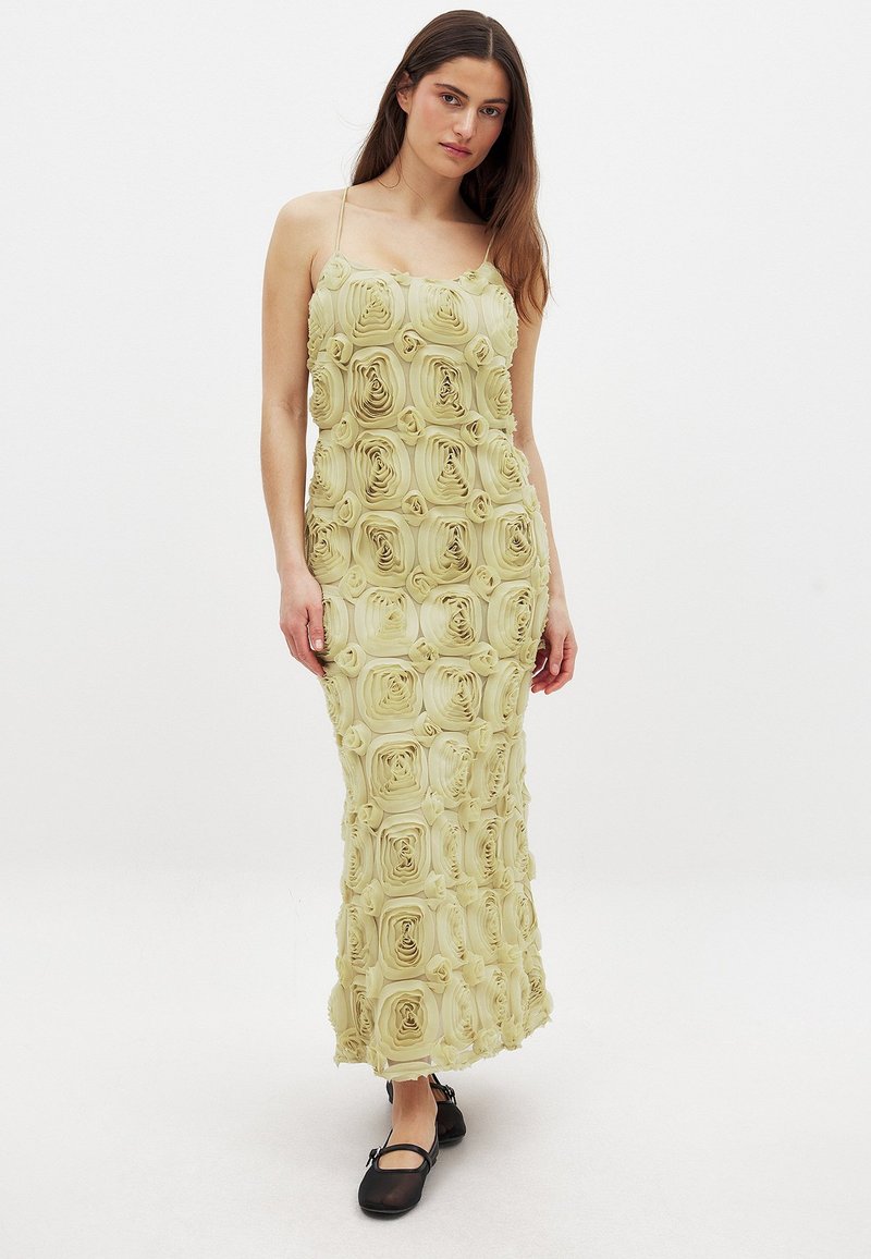 Robe maxi en vert clair avec une texture de pétales de rose. Dotée de bretelles fines et d'une silhouette ajustée, mettant en valeur des détails floraux tout au long.