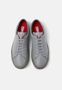 Sneaker in pelle grigia con sei fori per i lacci, lacci grigi e interno rosso. Punta arrotondata e suola in gomma verde a contrasto. Marchio Camper visibile.