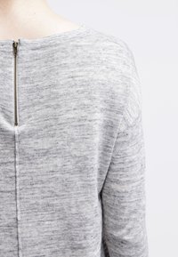 Lichtgrijze gebreide trui met een gestructureerd patroon, een ronde halslijn en een ritsdetail aan de achterkant van de nek.