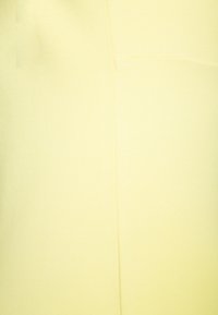 Gros plan sur un tissu jaune clair, texture lisse avec un éclat subtil, présentant un design simple et un minimum de détails de couture.