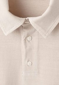 Beige polo tričko s klasickým límečkem, tříknoflíkovou légou a měkkou bavlněnou texturou. Viditelné švy na límečku a légě.
