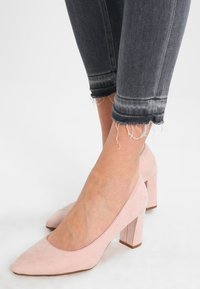 Różowe zamszowe szpilki na blokowym obcasie z ostrym noskiem, zestawione z poszarpanymi ciemnoszarymi dżinsami do kostek z frędzlami.