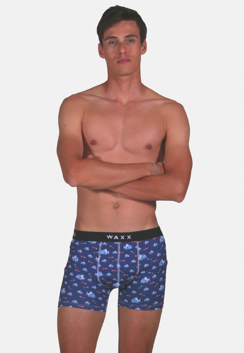 Caleçons boxers pour hommes en bleu marine avec un motif de poissons, dotés d'une taille noire portant le nom de la marque "WAXX". Matériau extensible, longueur jusqu'au milieux des cuisses.