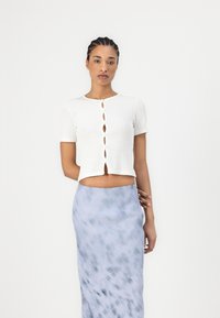 Haut blanc à rayures, à manches courtes, avec un col rond et une fermeture à boutons décoratifs. Associé à une jupe maxi tie-dye bleu clair.