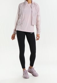Hellrosa Mesh-Jacke über einem hellrosanen Shirt, kombiniert mit schwarzen Leggings und helllila Sportschuhen. Einfaches, modernes Design.