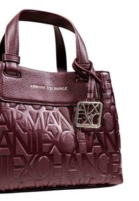 Sac à main bourgogne avec logo en relief, cuir texturé, poignées doubles et accents argentés avec les initiales de la marque.