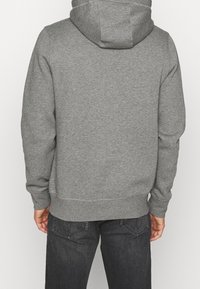 Sudadera gris hecha de un tejido suave y texturizado. Presenta una capucha con cordón y puños acanalados. Acabado liso sin logotipos o patrones visibles.