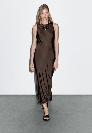Brown satin dress with a flowing silhouette, sleeveless design, and a glossy texture. Features a black necklace with round accents.