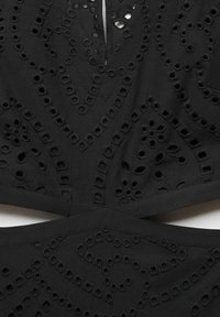 Vêtement noir présentant des motifs découpés complexes, une surface texturée et un design détaillé avec des formes géométriques et des éléments floraux.