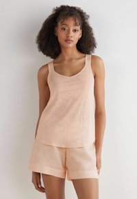 Persikofärgad linne med breda axelband och V-ringning, parat med matchande shorts som har en enkel nederkant. Tyget verkar lätt och texturerat.