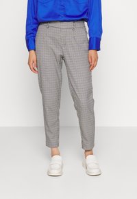 Chemise bleu satin à boutons, associée à un pantalon tapered à motif carreaux noir et blanc. Le modèle porte des mocassins blancs.
