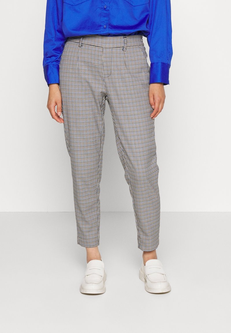 Chemise bleu satin à boutons, associée à un pantalon tapered à motif carreaux noir et blanc. Le modèle porte des mocassins blancs.