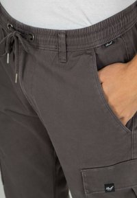 Graue, leichte Cargo-Hosen mit elastischem Bund, Kordelzugverschluss, Seitenaschen und einer aufgesetzten Tasche mit Markenlabel.