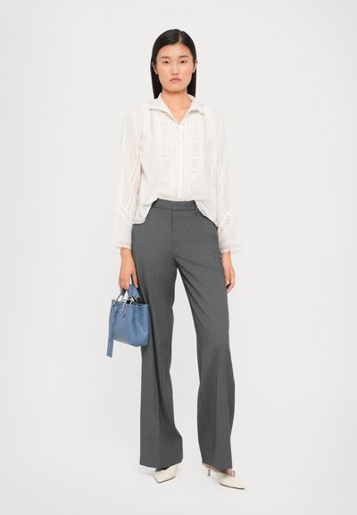 Blusa blanca con bordado, pantalones gris entallados y tacones puntiagudos en beige claro. Sosteniendo un pequeño bolso azul con detalle de etiqueta.