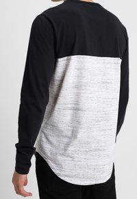 Pitkähihaiset paita, jossa musta yläosa ja tekstuurinen valkoinen vartalo harmailla suonilla. Pyöristetty helma, rento malli ja pehmeä kangas.