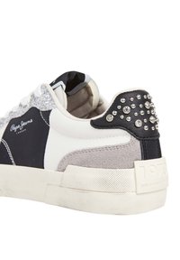Sneaker con una combinazione di pelle nera, pelle bianca e suede grigio, accentuato da borchie argentate sul tallone e una suola texture.