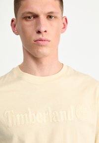 Beige katoenen t-shirt met reliëf 'Timberland' tekst en logo. Ronde hals met een soepele textuur en een standaard pasvorm.