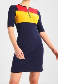 Marinblå klänning med en röd och gul färgblockerad topp, med en zippered halsringning och korta ärmar, tillverkad i ett stretchigt material.