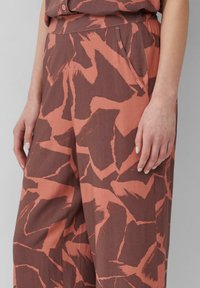 Losse pantalon in roestbruin met een abstract koraalpatroon, voorzien van een elastische tailleband, zijzakken en een gladde stoftextuur.