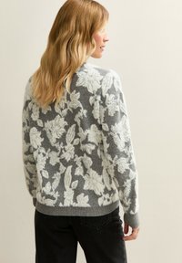 Suéter gris con estampado floral blanco, textura de punto y puños acanalados. El diseño trasero resalta el ajuste holgado.
