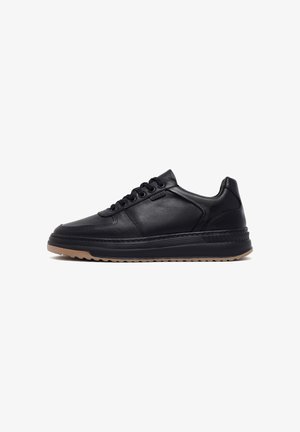 Zapatilla de cuero negro con punta redondeada, diseño de cordones y acentos texturizados. Cuenta con una suela de goma con una base en contraste de color marrón claro.