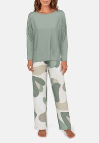 Šviesiai žalia ilgas rankoves turinti palaidinė su laisvu kirpimu, derinama su smėlio ir žaliais raštuotais pižamų kelnėmis, pagamintomis iš minkštos medžiagos. Nėra matomų logotipų.