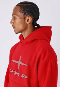Sudadera roja con una gran estrella plateada y el logo "PXR" en el pecho, con un tejido texturizado y capucha con cordón.