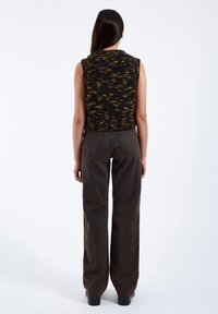 Svart och gult prickig ärmlös stickad topp som matchas med högmidjade, löst sittande mörkgrå jeans. Enkelt och strukturerat mönster.